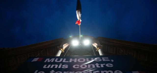 Message lumineux projeté sur la façade d'une mairie et surplombé d'un drapeau français en berne