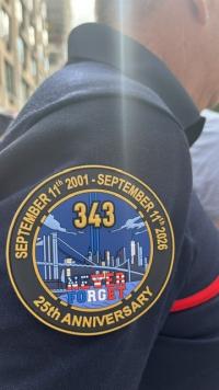 Ecusson commémoratif pour les 25 ans du 11-Septembre porté sur le bras droit d'un pompier français avec notamment la mention Never Forget