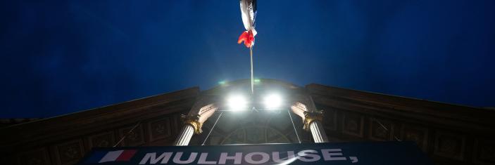 Message lumineux projeté sur la façade d'une mairie et surplombé d'un drapeau français en berne